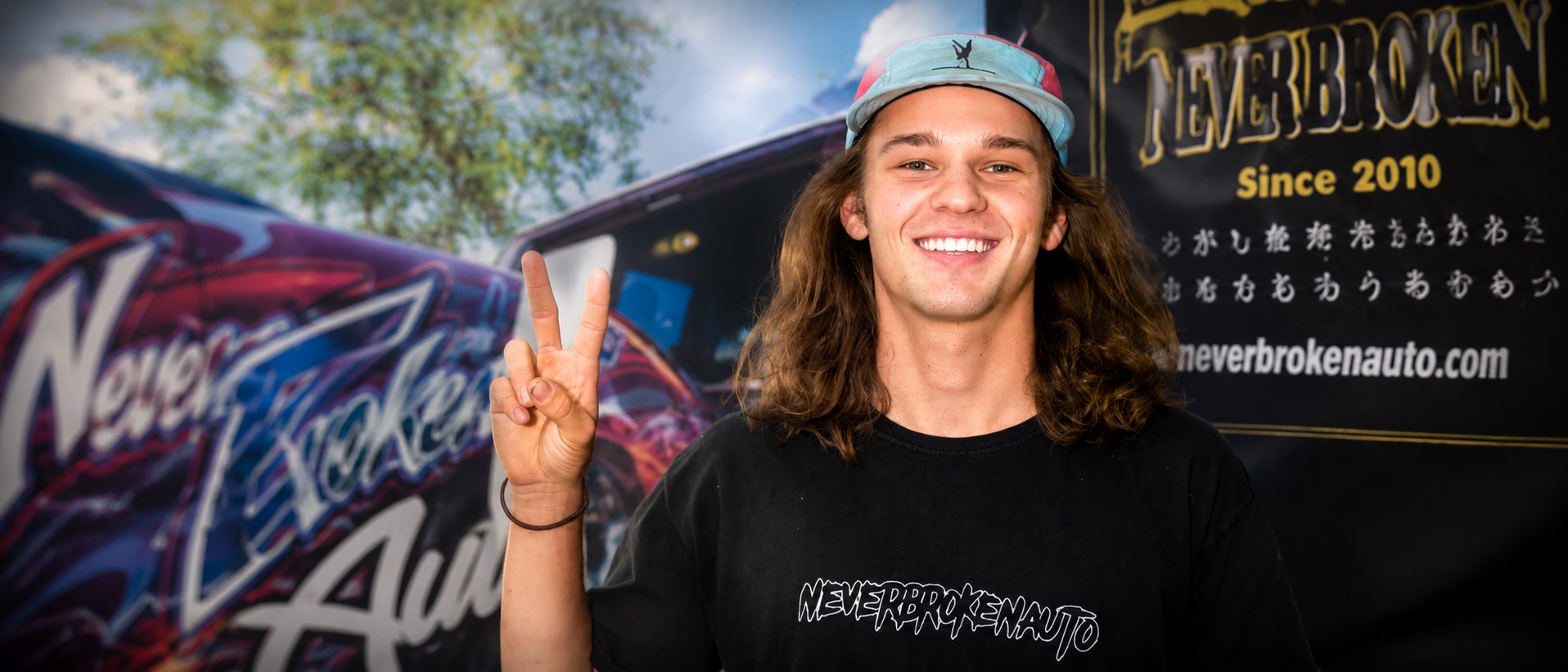 Kelton, founder of NBAUTOAZ, in front of Never Broken Auto graphics
